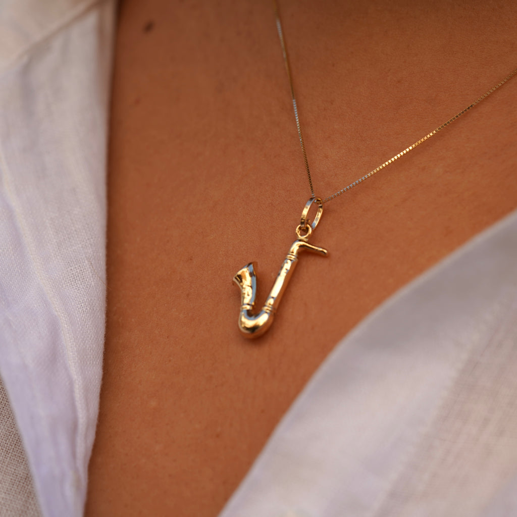 Model wearing the 14K Gold Saxophone Charm on a chain, showcasing its intricate musical instrument design and polished yellow gold finish.