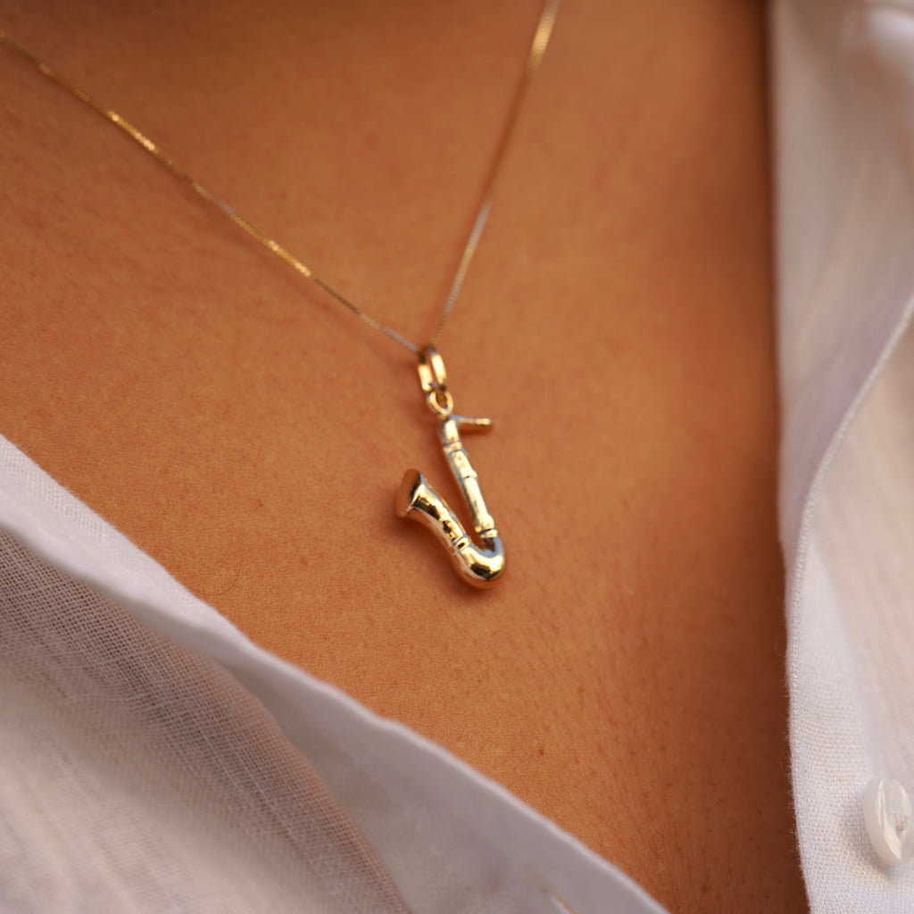 Model wearing the 14K Gold Saxophone Charm on a chain, showcasing its intricate musical instrument design and polished yellow gold finish.